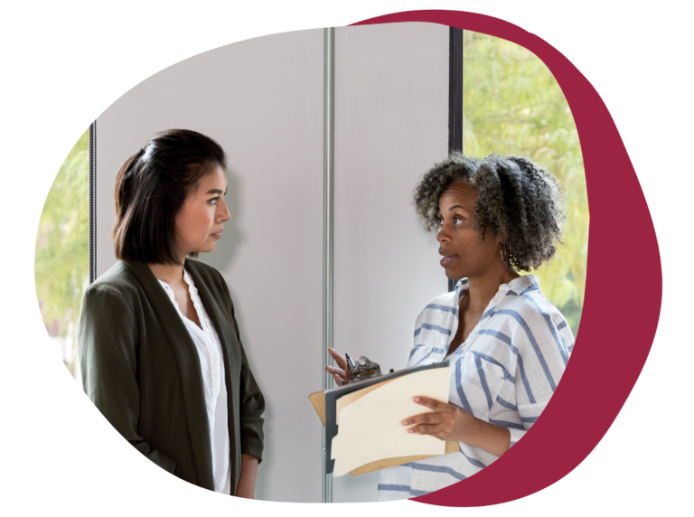 professional women discussing ideas in an office setting with a clipboard and natural light, diverse conversation with a clipboard