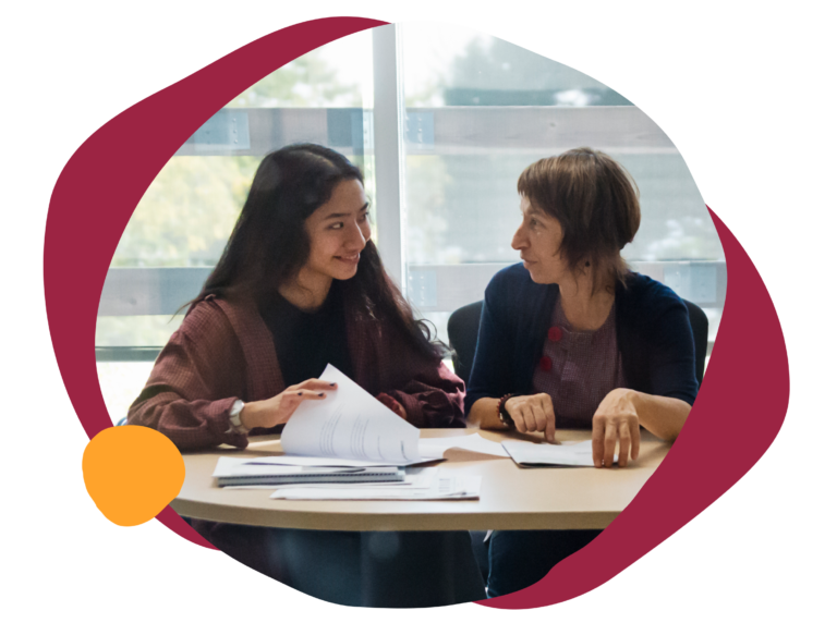 collaborative discussion between two women at a table, sharing documents in a bright, modern workspace, students discussing academic materials