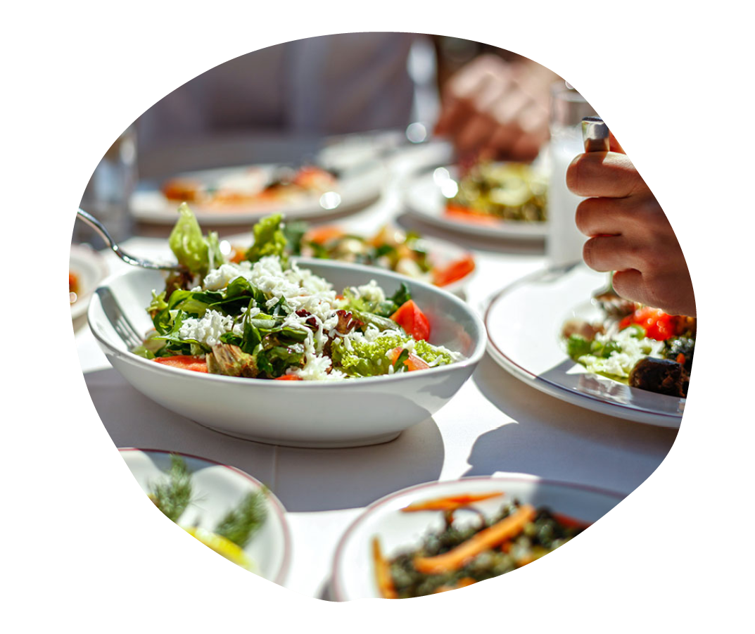 salad with fresh greens and tomatoes at a dining table, surrounded by plates of colorful dishes, outdoor dining experience in sunlight