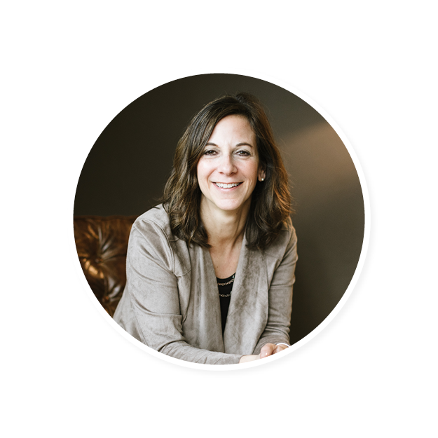 woman smiling in a circular frame, wearing a gray blazer, seated, warm lighting, relaxed atmosphere, professional portrait of a woman with brown hair, casual setting, inviting smile