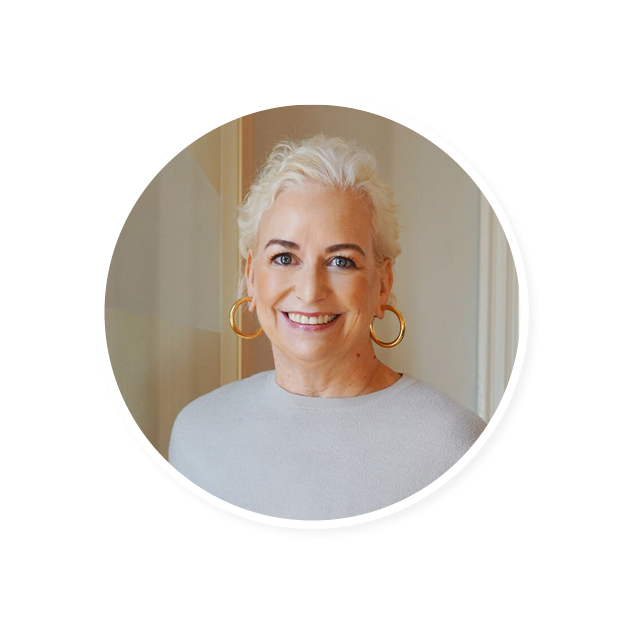 smiling woman with short, wavy white hair and gold hoop earrings wearing a light sweater in a softly lit room, portrait of a confident woman showcasing a warm smile and stylish accessories