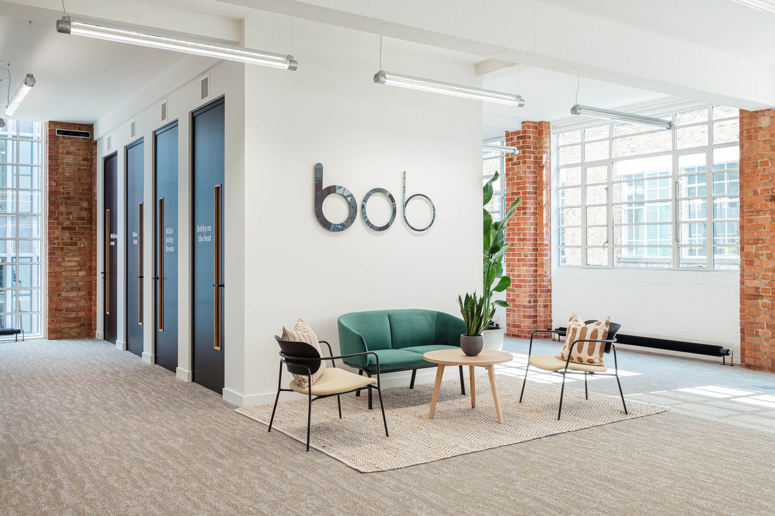 modern office lobby with green sofa, wooden table, and natural light; stylish decor and vibrant brick walls, contemporary workspace featuring seating area and meeting rooms