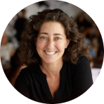 portrait of a smiling woman with curly hair, casual setting with blurred background elements