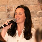 smiling woman holding microphone on stone wall background, speaker engaging audience with clear expression during event