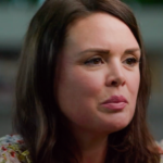 woman with long brown hair, soft expression, wearing floral top, engaged in conversation, background slightly blurred, floral fashion, candid portrait, thoughtful expression, warm ambiance