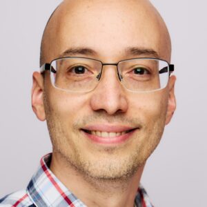 bald man with glasses smiling in a plaid shirt against a light background, friendly professional portrait with glasses and plaid shirt